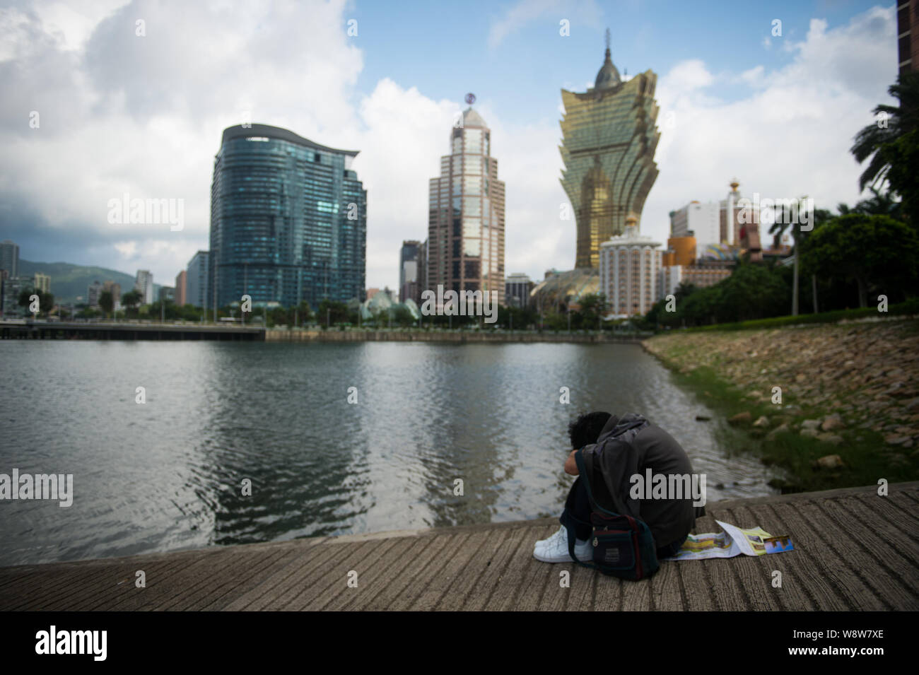 --FILE--A tourist rests by a river bank in front of the Grand Lisboa casino, right, and other casinos in Macau, China, 29 May 2014.   The worlds casin Stock Photo