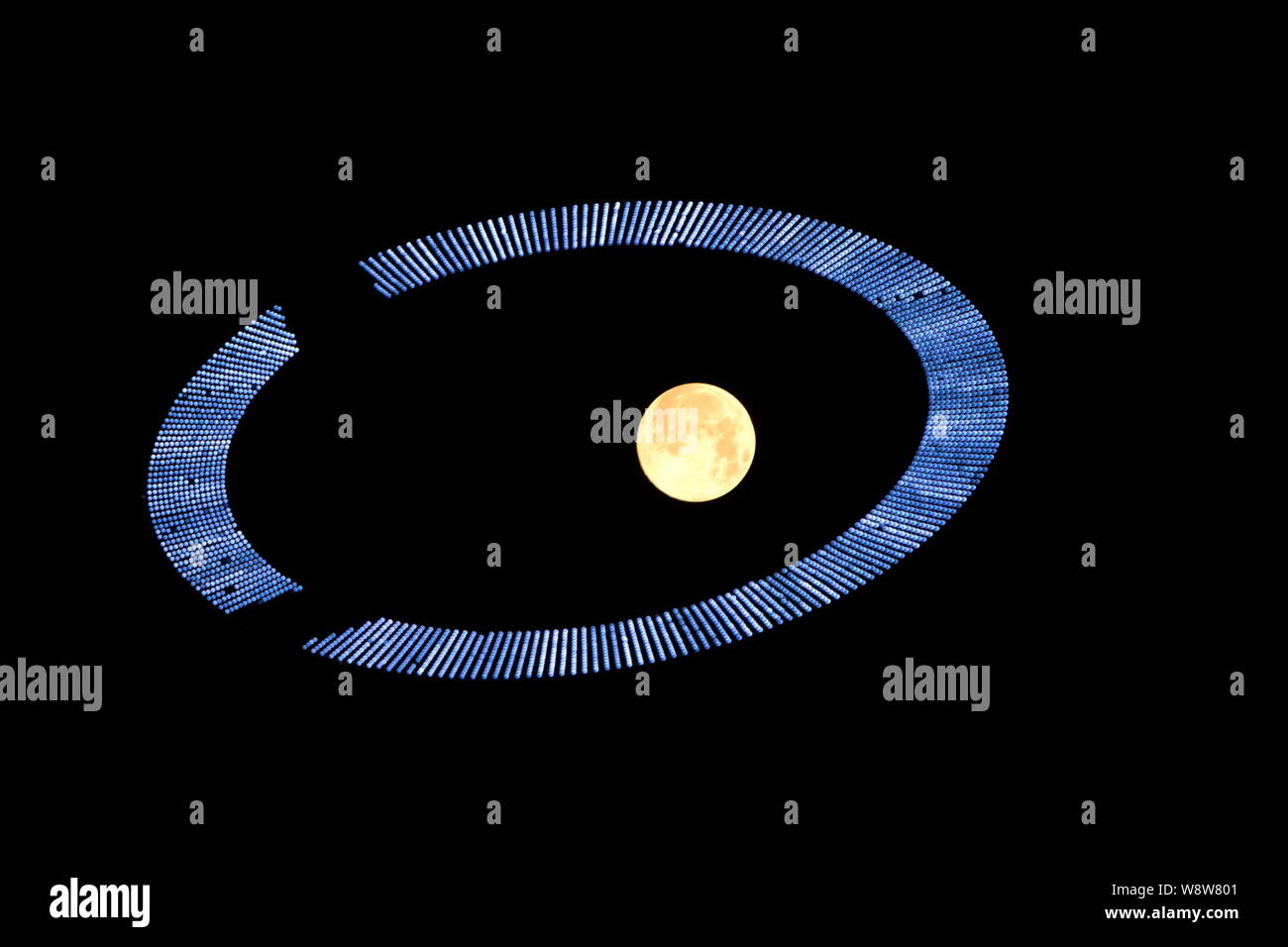 The full moon is seen through one of the Olympic rings on display at