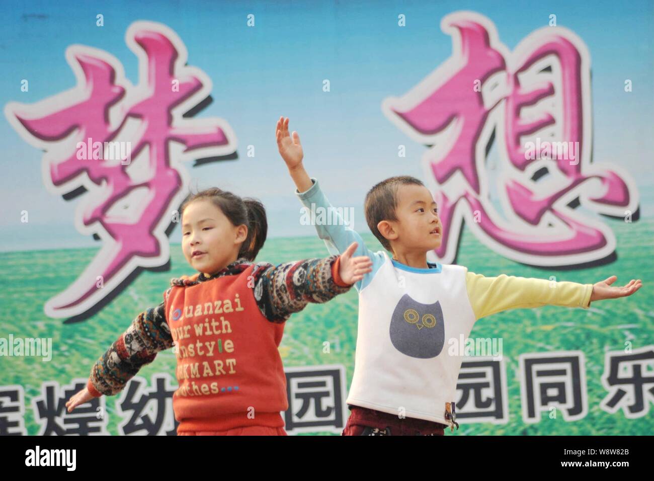 Young Chinese children left behind by their migrant worker parents play games in front of a Chinese sign meaning 'dream' at a rural kindergarten in Xi Stock Photo