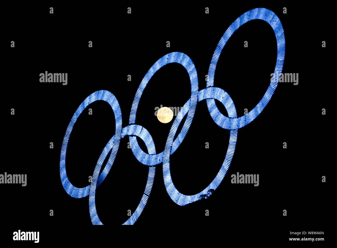 The full moon is seen through the Olympic rings on display at the