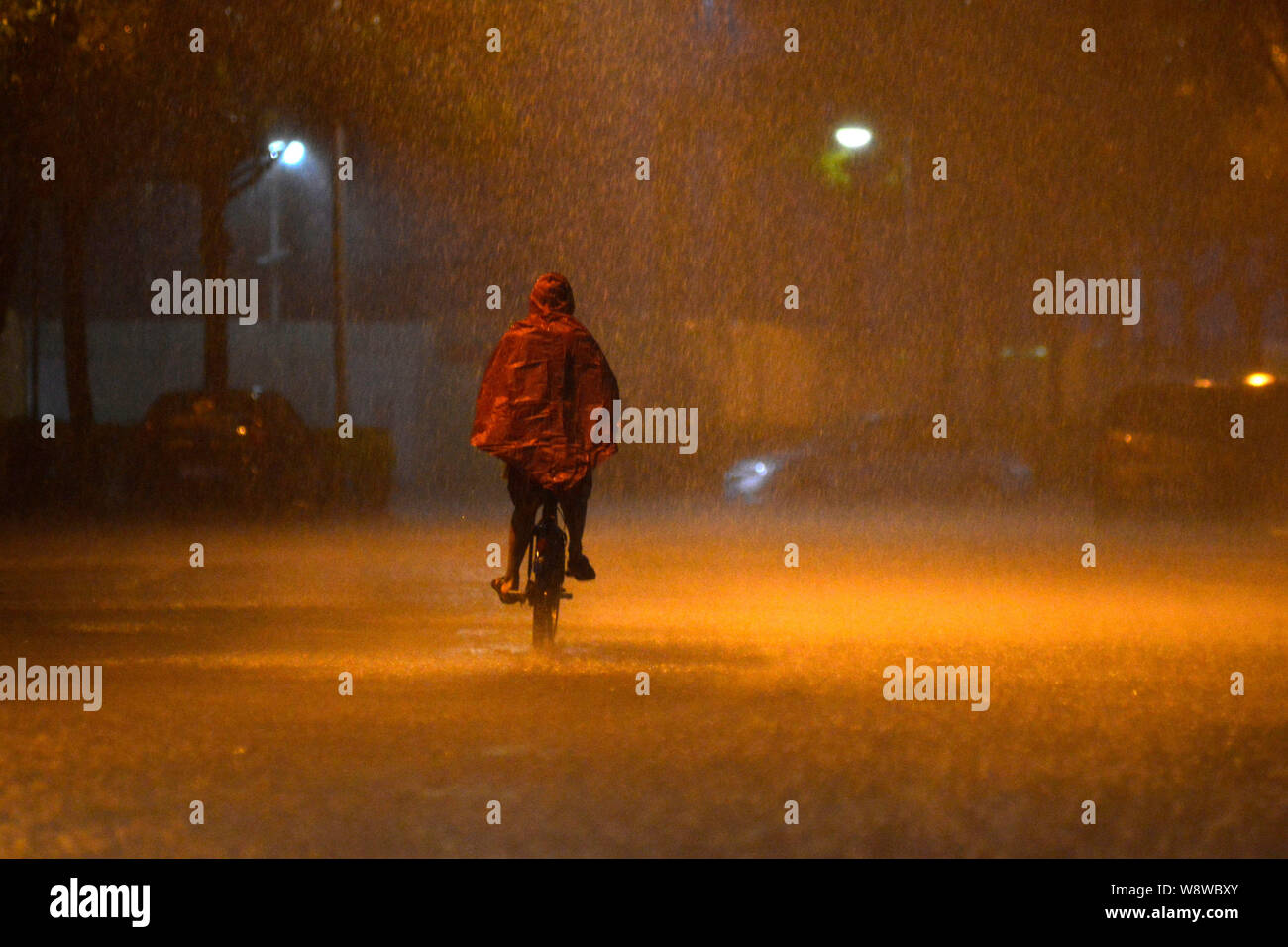 A cyclist rides in heavy rain on a road in Shenzhen city, south Chinas Guangdong province, 30 March 2014.   Heavy rains have grounded flights and stra Stock Photo