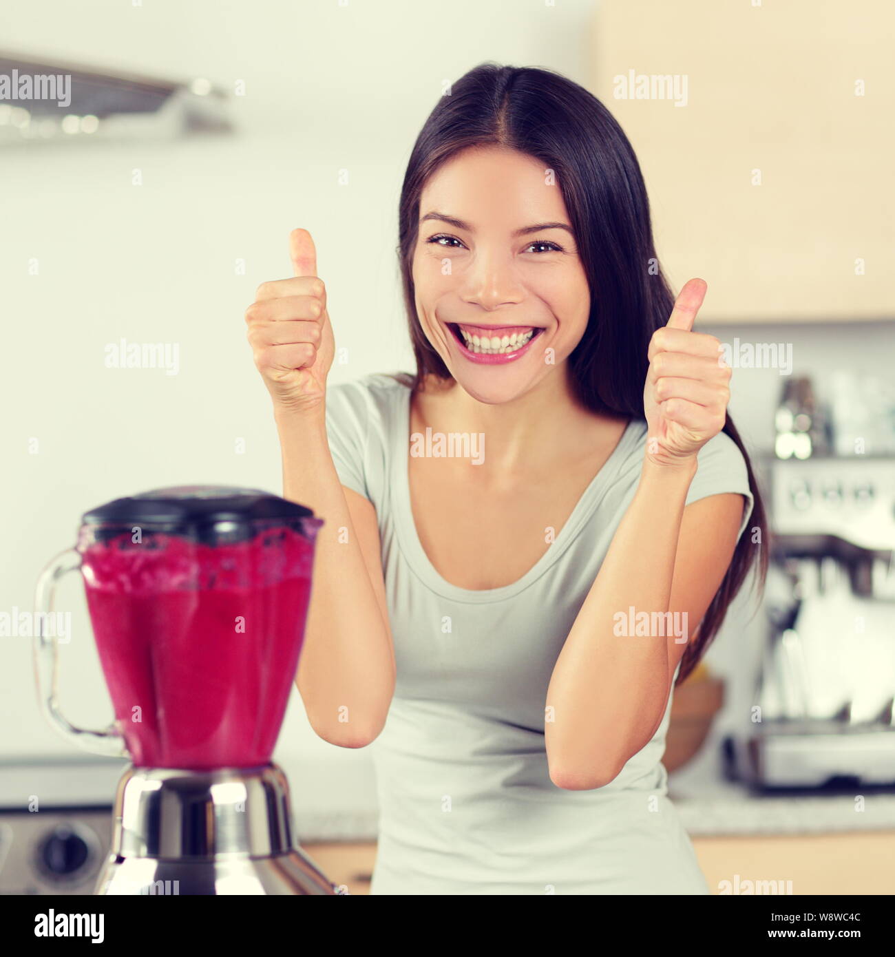 Smoothie woman making fruit and berry smoothies giving thumbs up happy by blender. Healthy eating lifestyle concept portrait of beautiful young woman preparing drink blending strawberries, raspberries Stock Photo