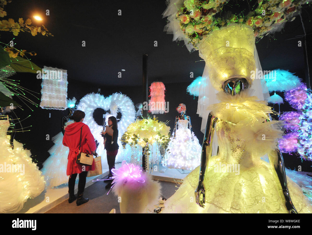 A Chinese employee talks with a visitor next to illuminated fibre optic wedding dresses on display at the China Wedding Expo 2014 in Shanghai, China, Stock Photo
