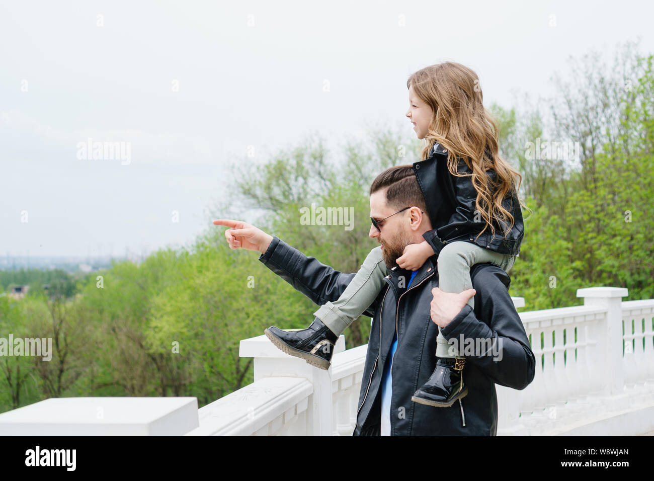Fashionable stylish family for a walk. Dad rolls his daughter on his shoulders. Excursion. Indicate the direction.Travel and tourism concept. Time tog Stock Photo