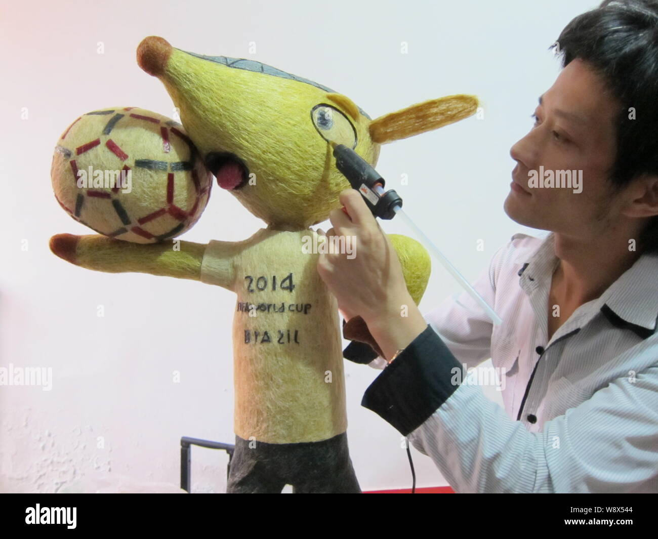 Chinese hairstylist Huang Xin puts final touches on his hair-made Fuleco, the mascot of the 2014 FIFA World Cup Brazil, in Beijing, China, 8 May 2014. Stock Photo