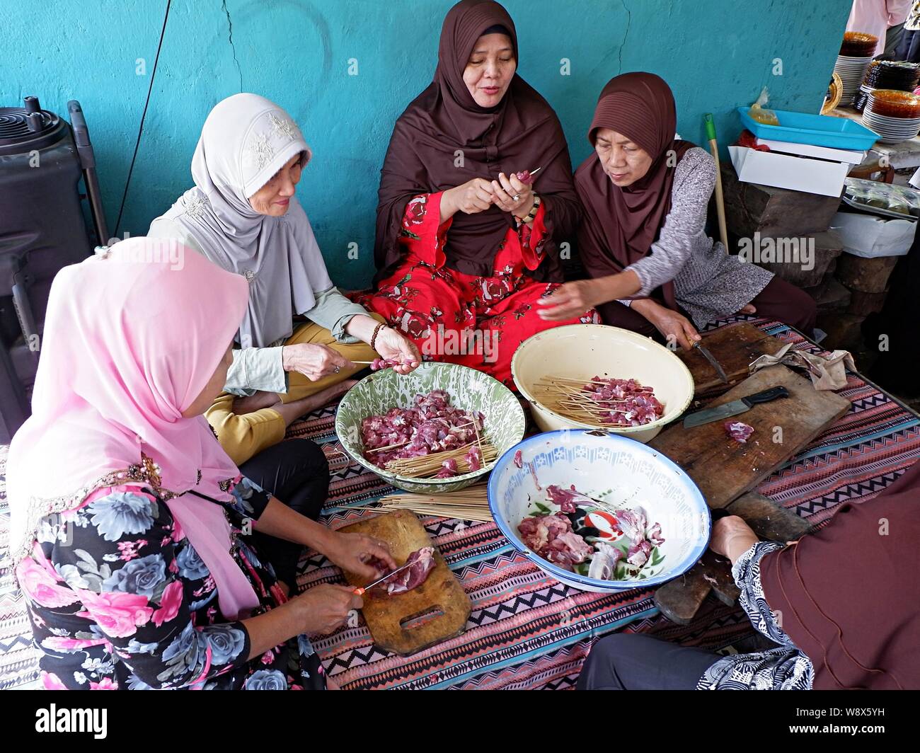 A group of muslim women (muslimah) prepare raw mutton satay and ingredients together. Stock Photo