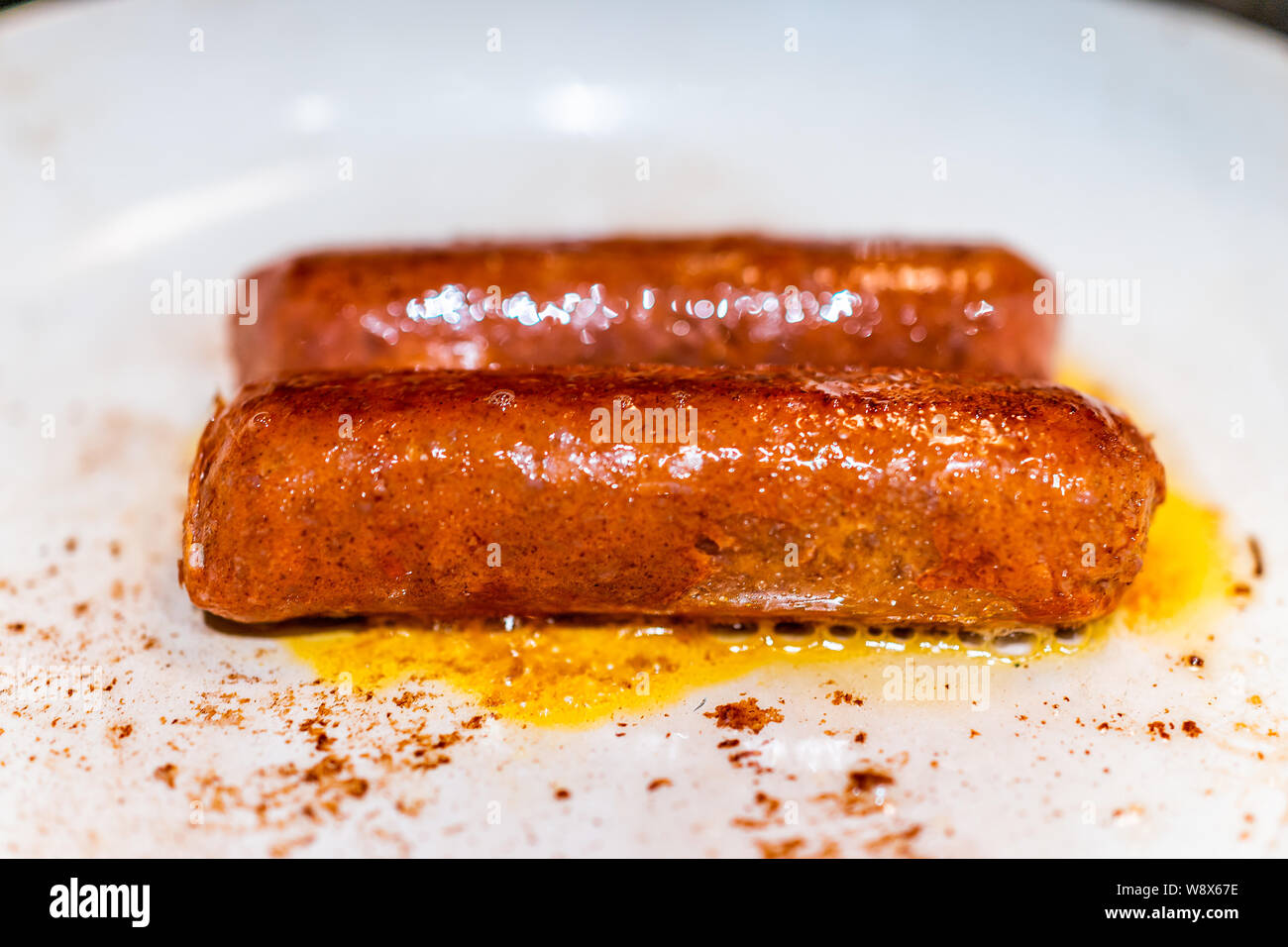 Closeup of two vegan meat sausages cooking on ceramic nonstick frying pan Stock Photo