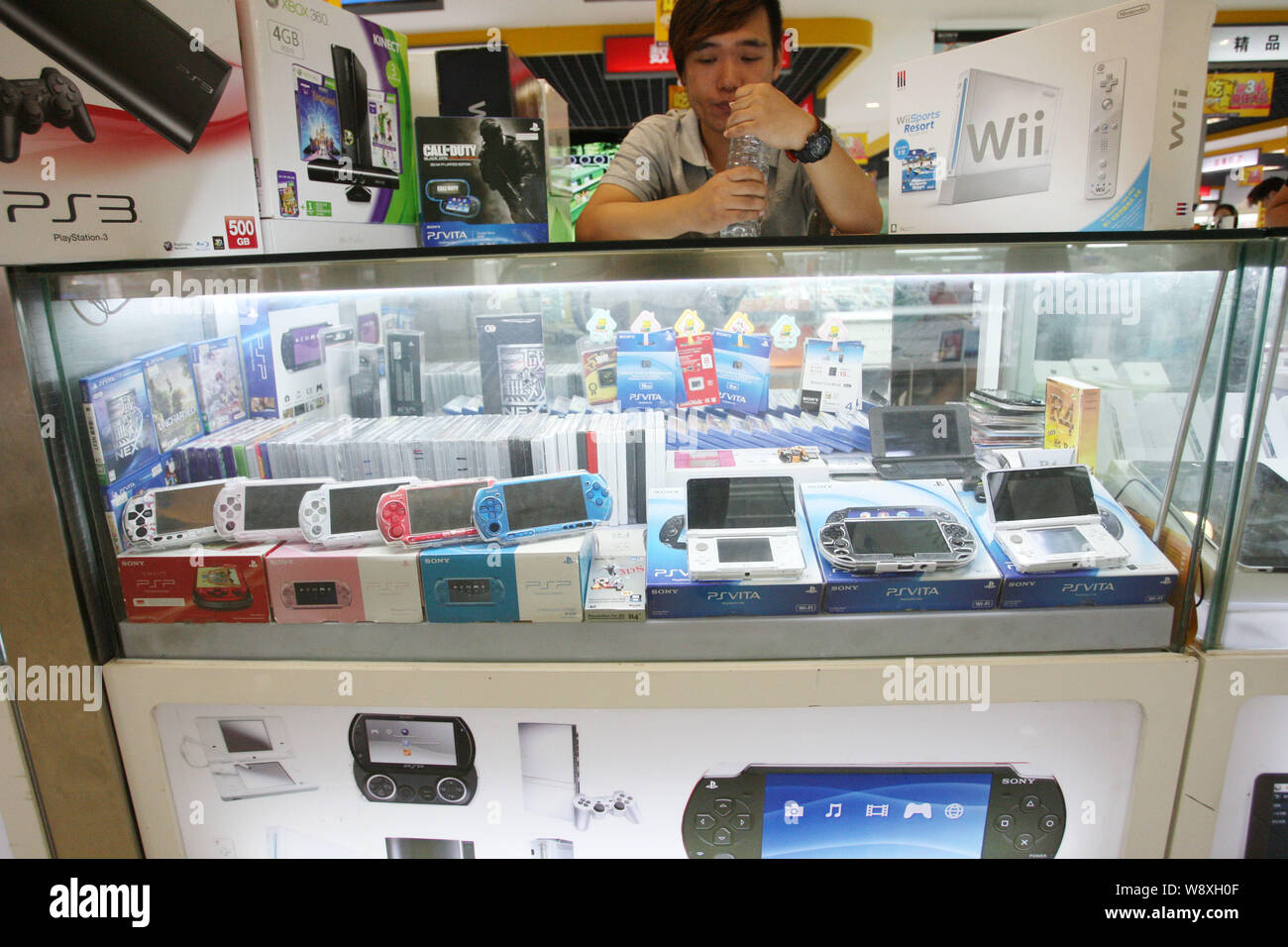 --FILE--A salesman looks at Sony PSVita and PSP game consoles for sale at a stall in a digital products mall in Shanghai, China, 10 July 2013.   After Stock Photo