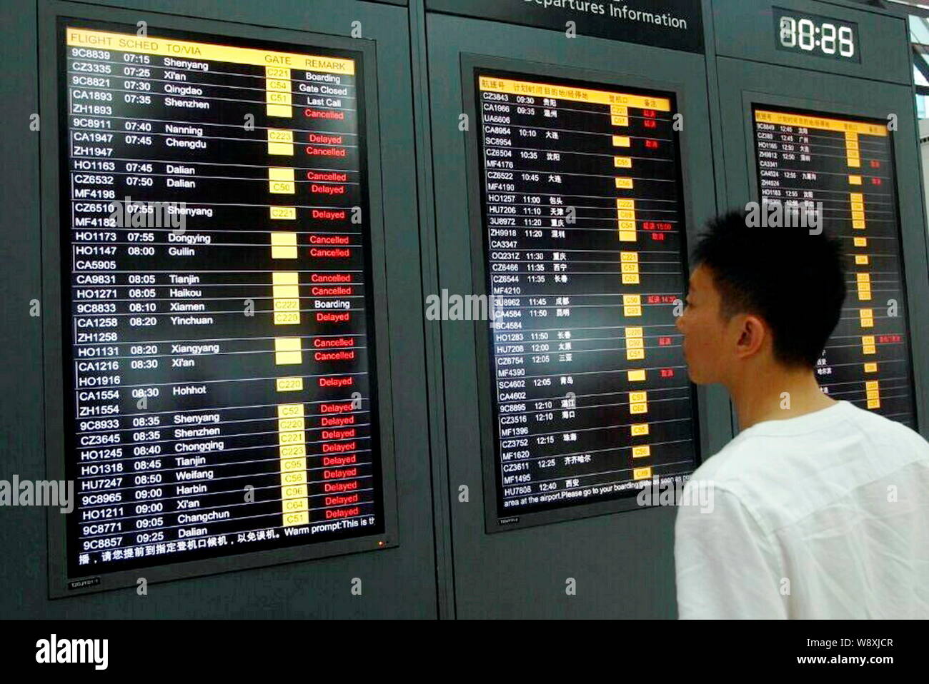 A passenger watches displays showing departure information of flights, most of which were cancelled or delayed due to Typhoon Fung-Wong, at the Termin Stock Photo