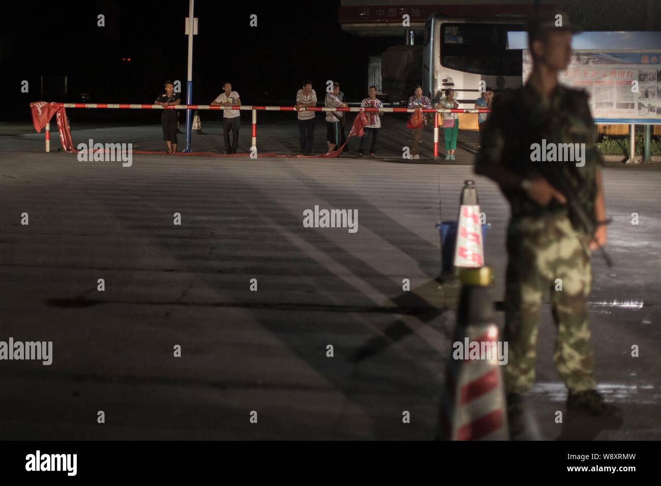 An armed Chinese frontier policeman stands guard near a group of passengers as their bus is being searched for drugs at a checkpoint in Xishuangbanna, Stock Photo