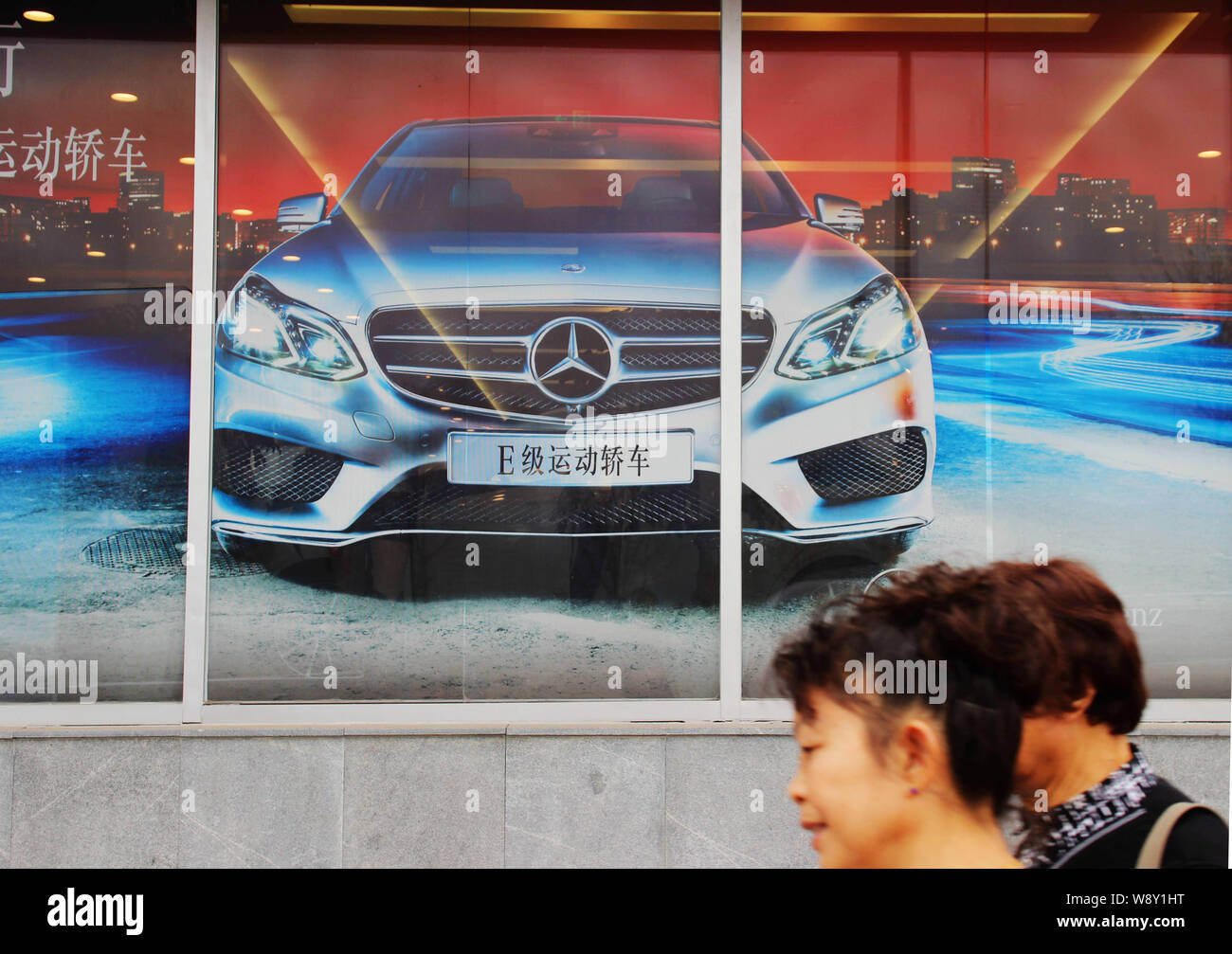 --FILE--Pedestrians walk past an advertisement for Mercedes-Benz E-Class cars in Chongqing, China, 18 November 2013.   Mercedes-Benz may be one of the Stock Photo