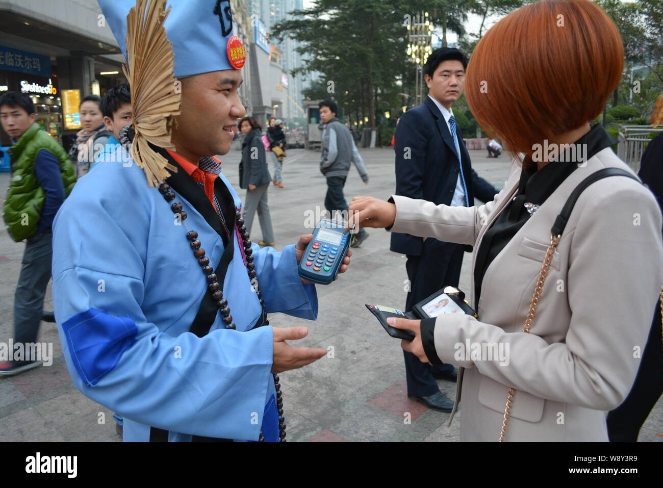 a-pedestrian-right-swipes-her-credit-card-on-the-pos-machine-of-chinese-businessman-wang-jiang-left-dressed-like-a-beggar-in-a-costume-of-chinese-W8Y3R9.jpg