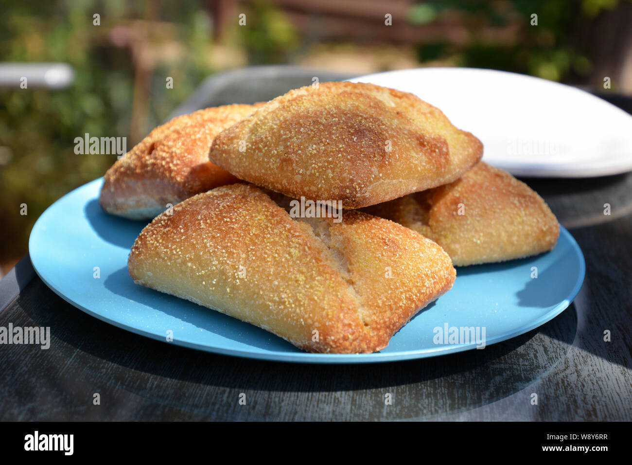Fresh crusty bread rolls piled up on a blue plate on outdoor table Stock Photo