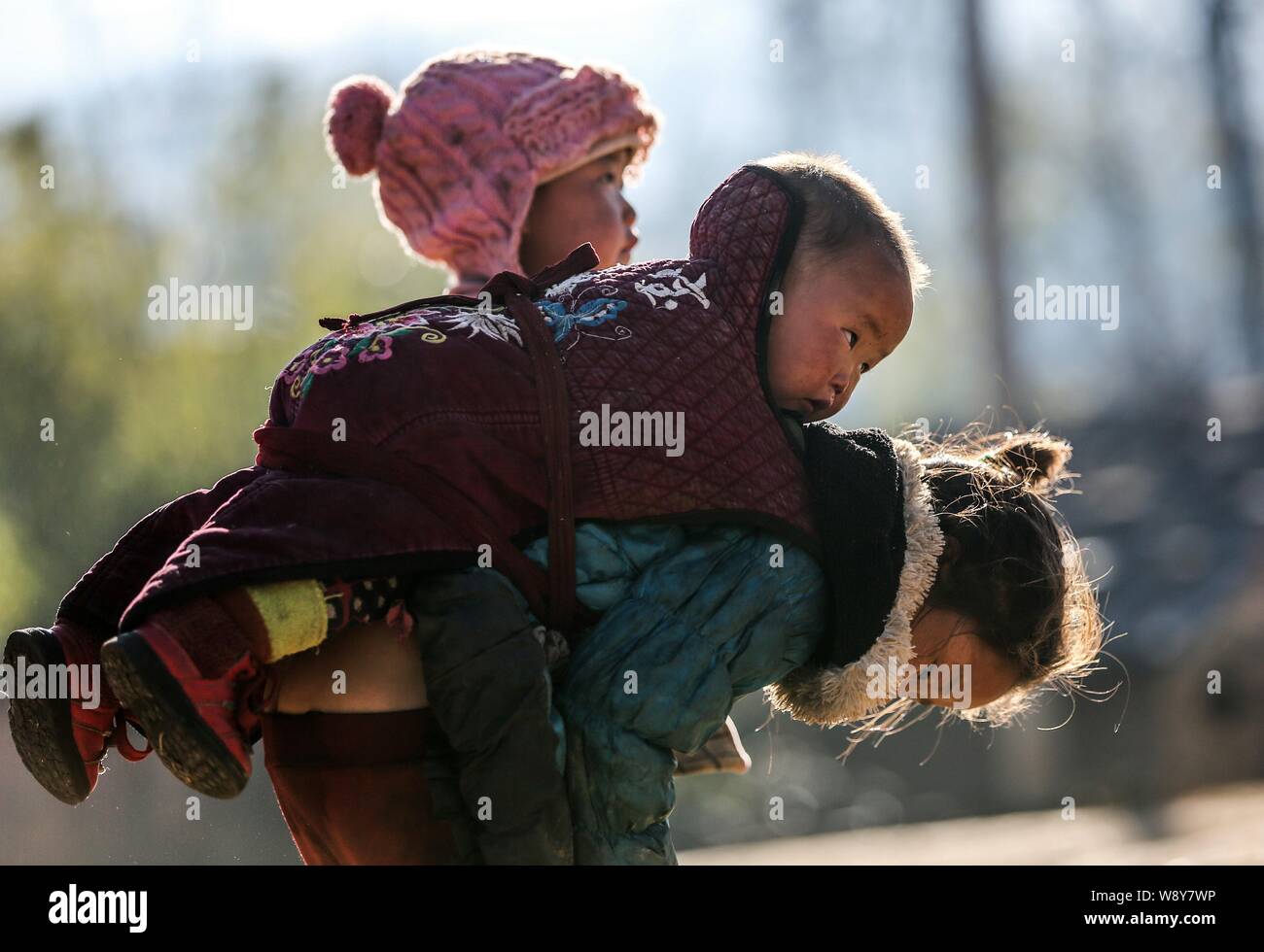 A six-year-old girl carries her months-old brother on the back while she is working in the farm field in a poor village in Daliang Mountain in Liangsh Stock Photo