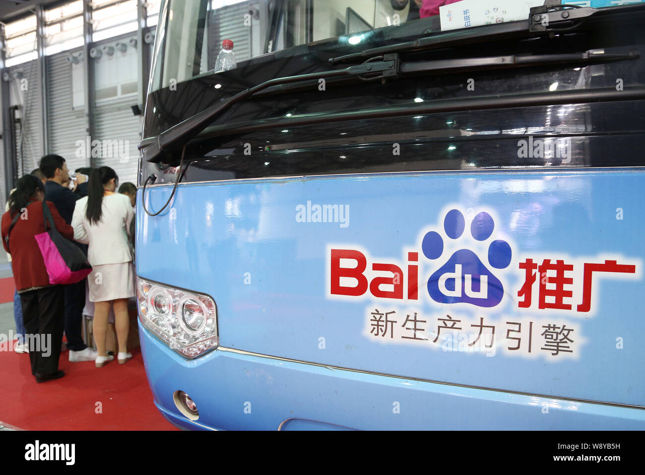 --FILE--Visitors stand next to a passenger bus with an advertisement for Baidu during the 16th China International Industry Fair (CIIF) in Shanghai, C Stock Photo