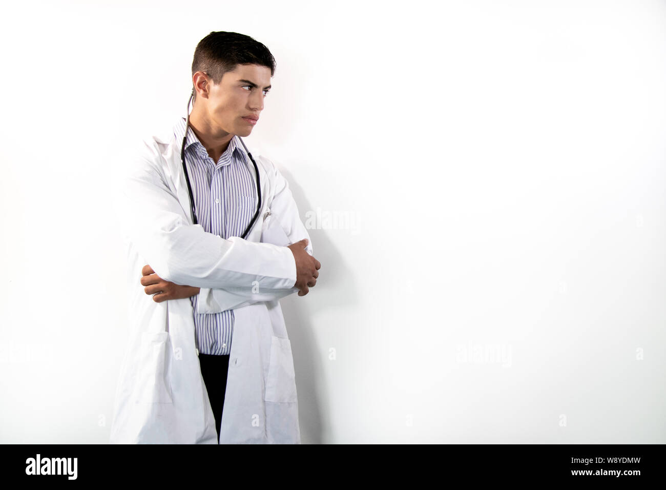 Handsome doctor wearing white lab coat with folded arms looking aaway