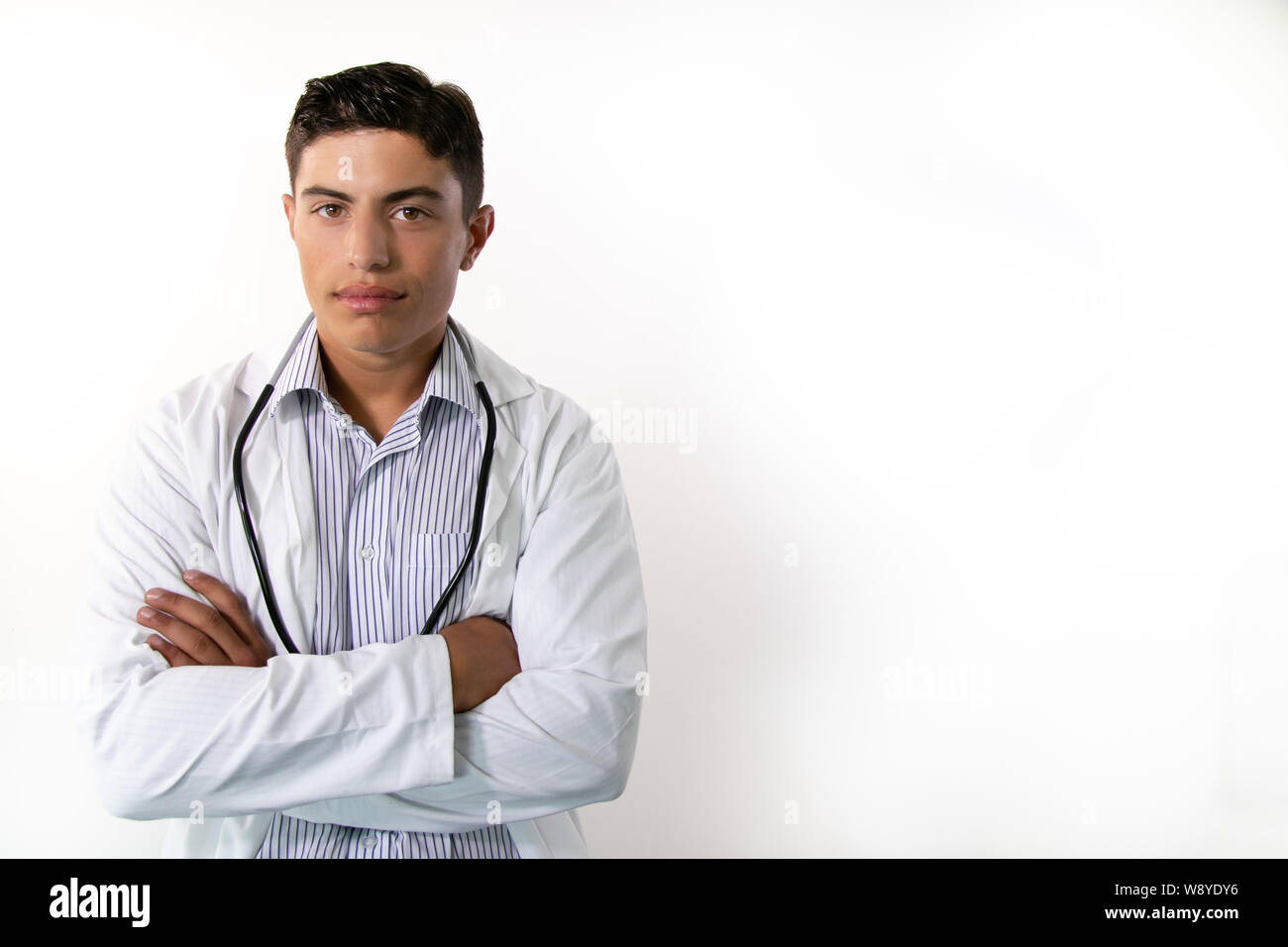 Handsome doctor wearing white lab coat with folded arms looking at