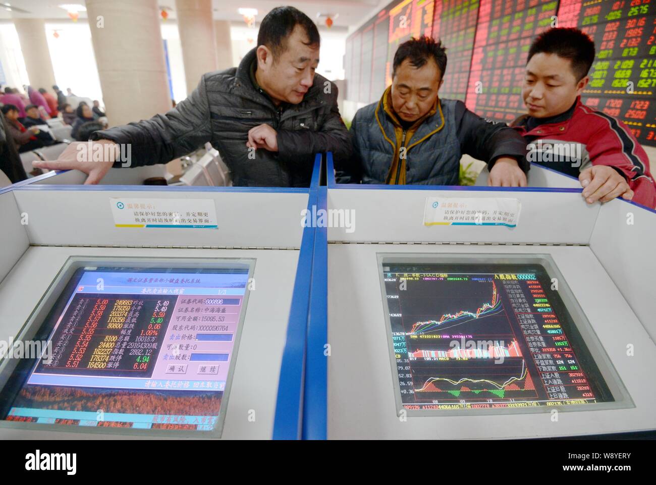 Chinese investors watch computer displays showing prices of shares (red for price rising and green for price falling) and the Shanghai Composite Index Stock Photo