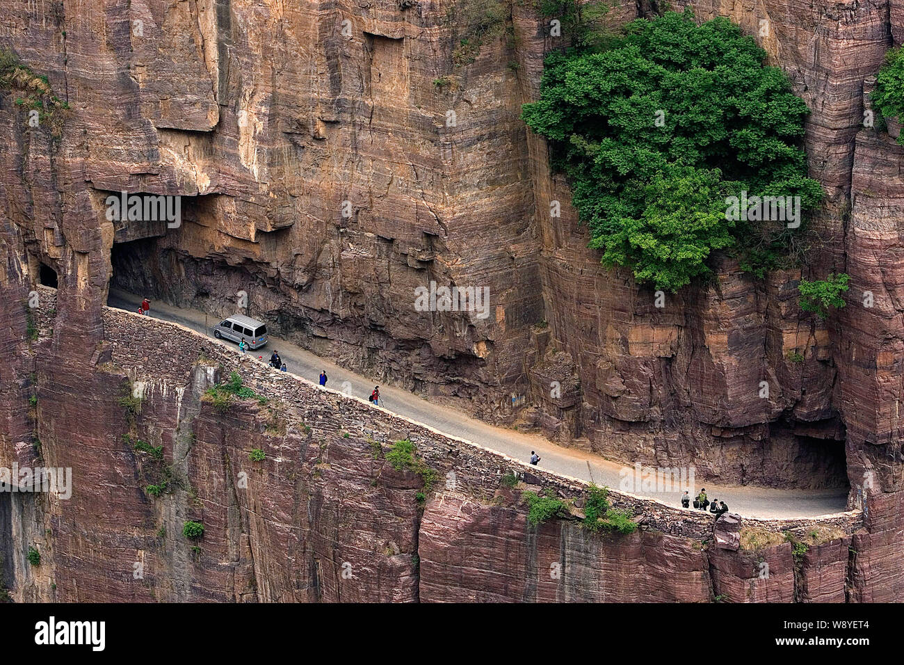 --FILE--A minivan passes by people wallking along the Guoliang Tunnel through the Wanxian Mountain in the Taihang Mountains in Huixian county, Xinxian Stock Photo