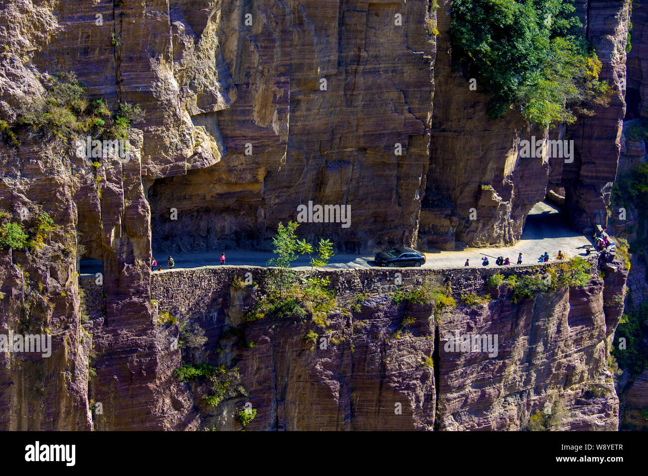 Tourists and a car pass along the Guoliang Tunnel through the Wanxian Mountain in the Taihang Mountains in Huixian county, Xinxiang city, central Chin Stock Photo