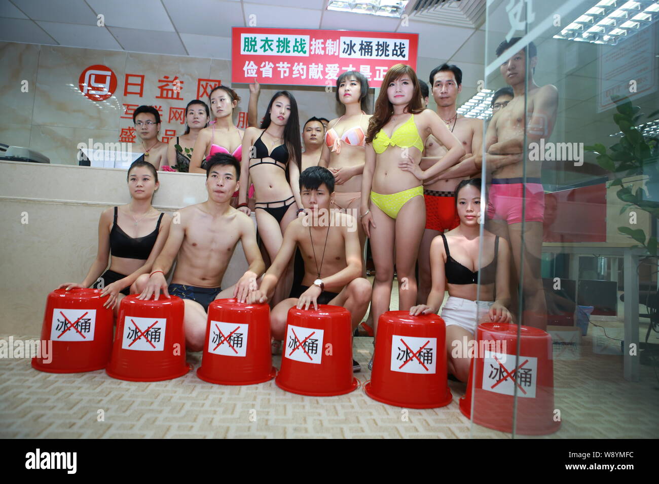 Chinese employees dressed in bikinis and swimming trunks pose behind empty buckets to boycott the Ice Bucket Challenge at their office in Shenzhen cit Stock Photo