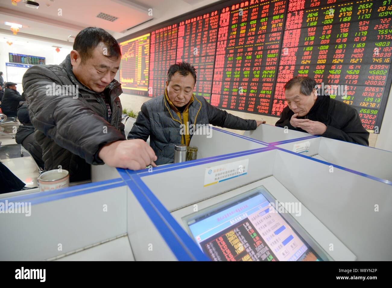 Chinese investors watch computer displays showing prices of shares (red for price rising and green for price falling) at a stock brokerage house in Fu Stock Photo