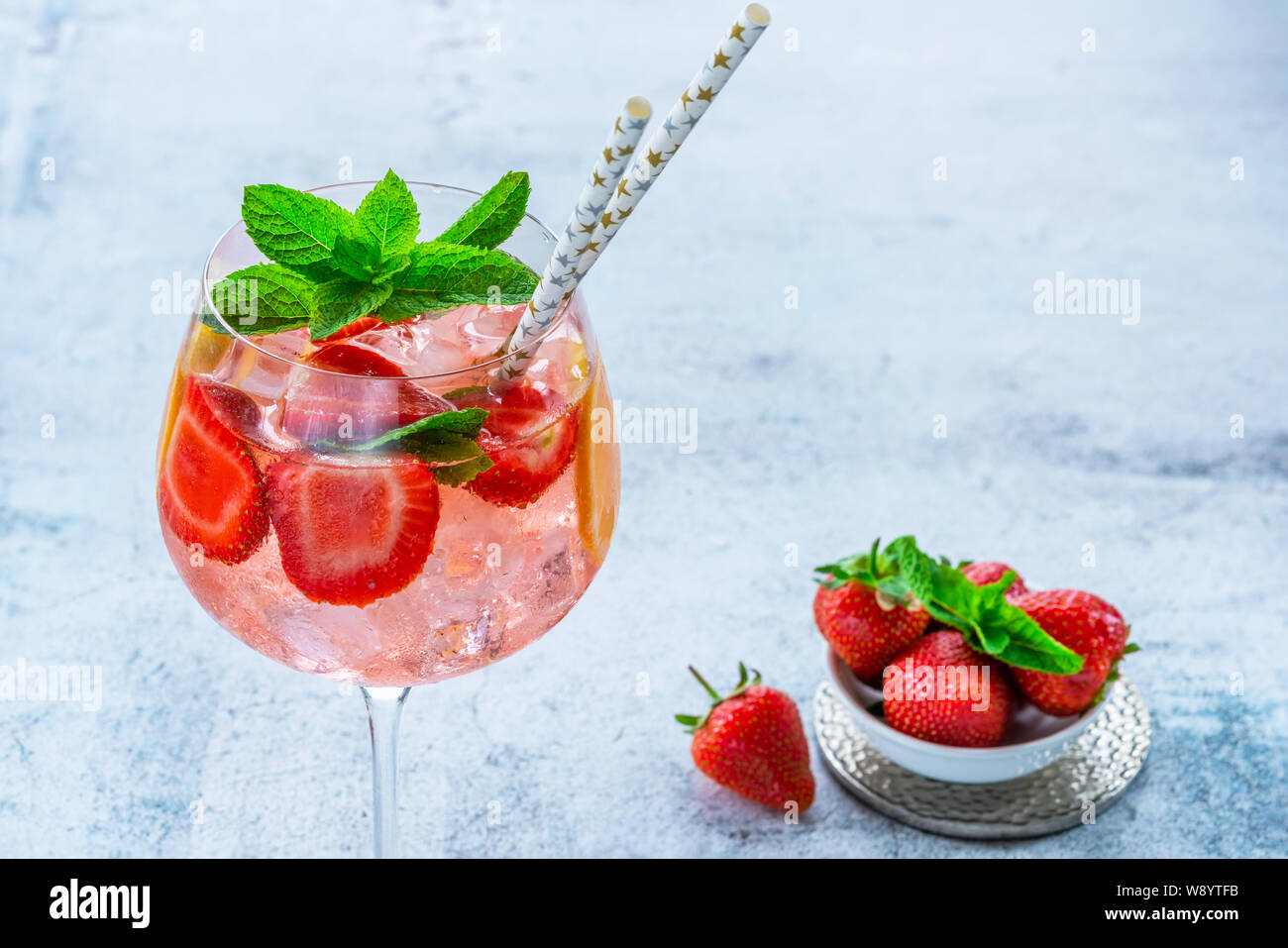 Pink gin and tonic cocktail with prosecco and strawberries, garnished