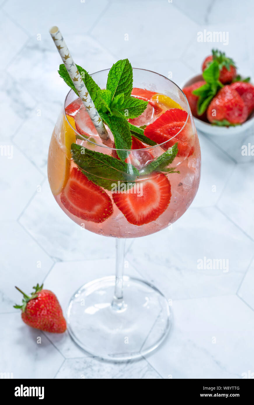Pink gin and tonic cocktail with prosecco and strawberries, garnished