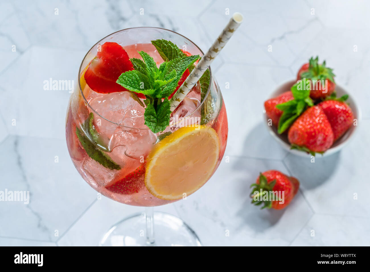 Pink gin and tonic cocktail with prosecco and strawberries, garnished