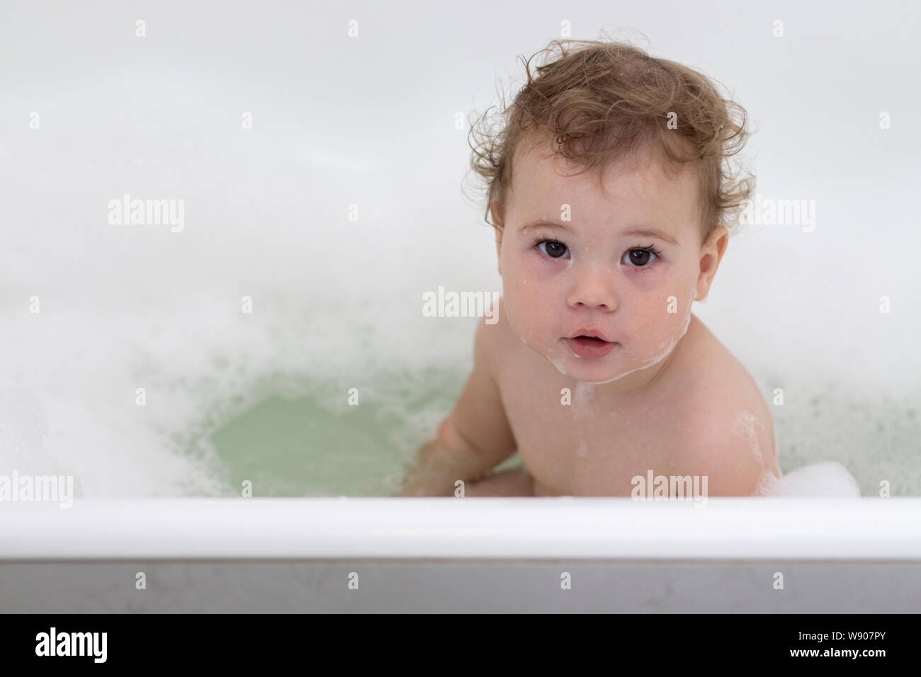 A 1 year old Caucasian child washes in the bath, a girl boy sits in the water with foam