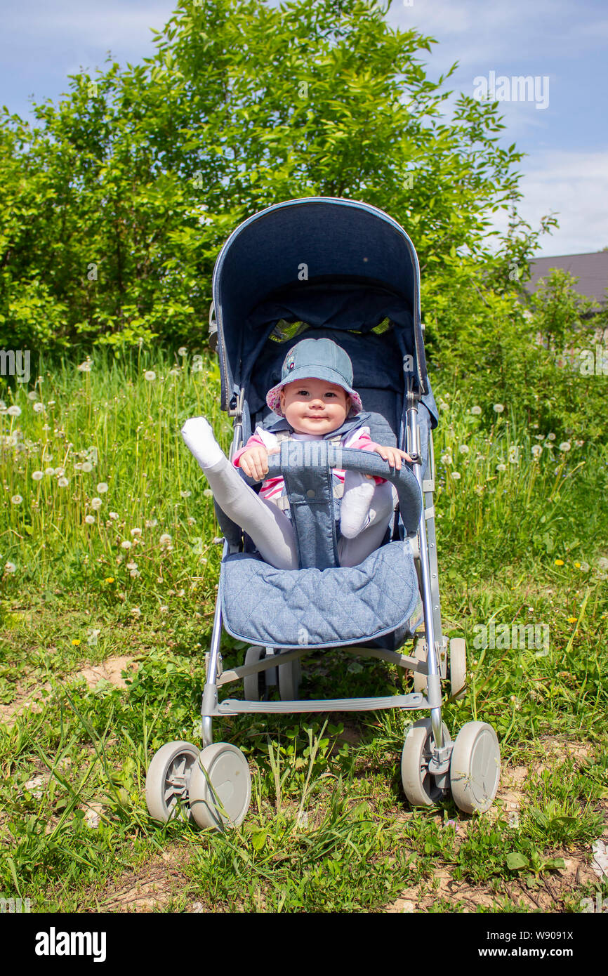 A 9 month old girl sits in a summer carriage and plays with her legs. Little smiling child in a hat on a walk sunny summer day Stock Photo Alamy