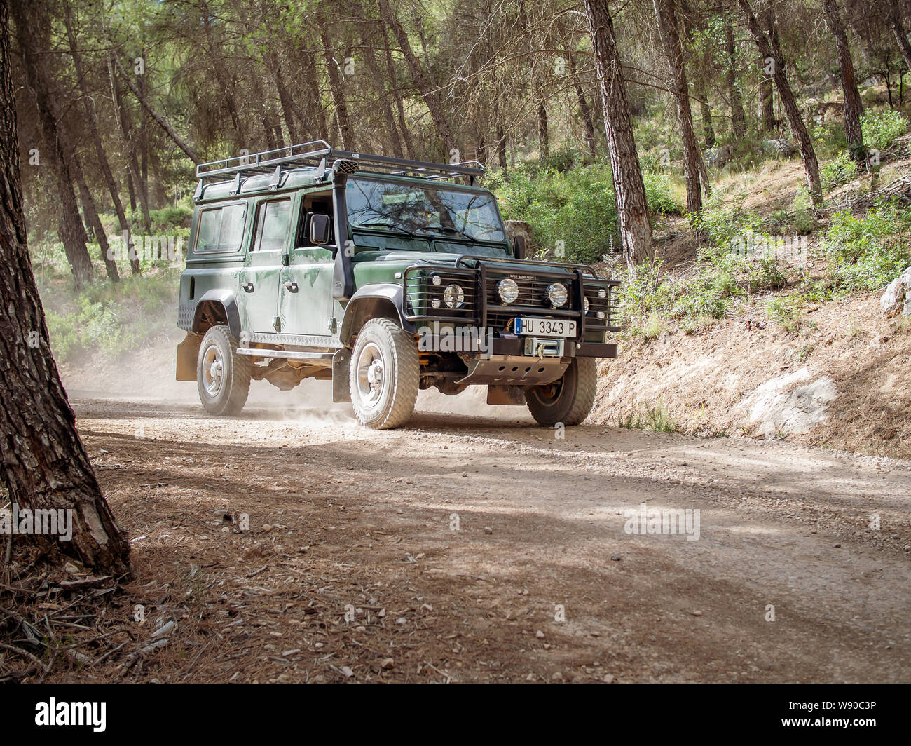 MONTFALCO, SPAIN-AUGUST 12, 2019: Green Land Rover Defender 110 riding a dusty forest road Stock Photo