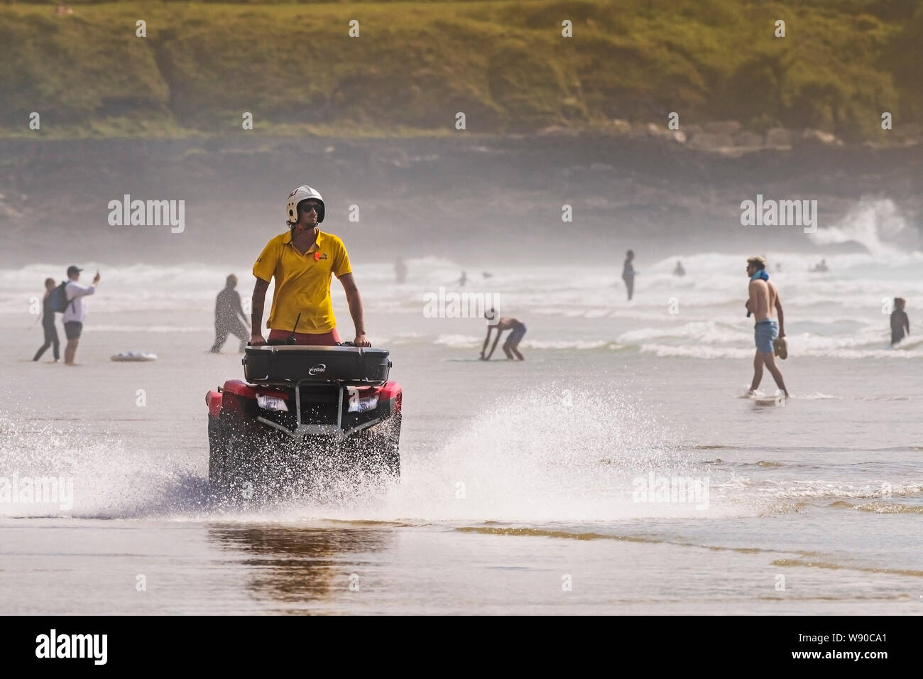 A RNLI Lifeguard riding a quadbike and patrolling along the shoreline at Fistral Beach in Newquay in Cornwall. Stock Photo