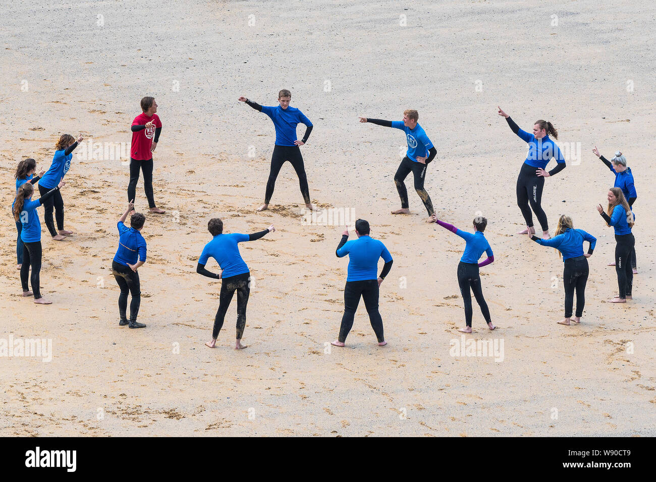 Novice surfers warming up before a surfing lesson on Great Gt. Western Beach in Newquay in Cornwall. Stock Photo