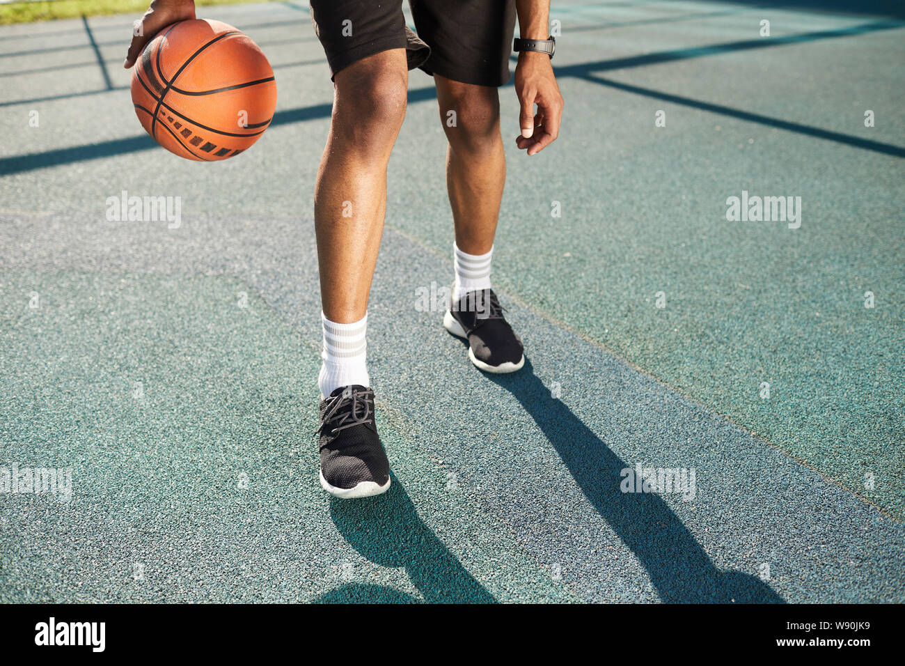 Muscular legs of unrecognizable basketball player training in outdoor court, copy space Stock Photo