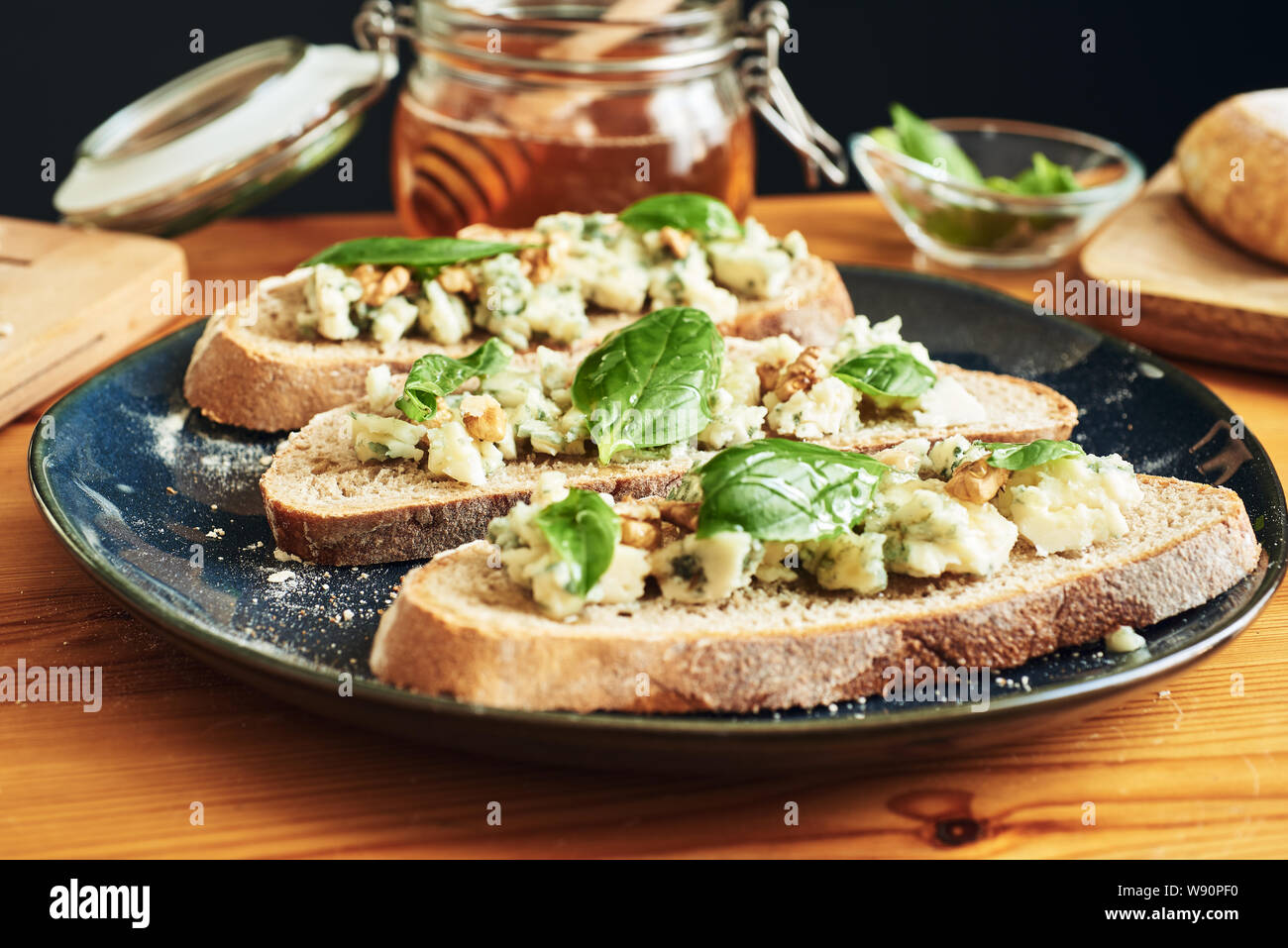 Close up on a plate of toasts with roquefort cheese, walnuts, honey and basil. Selective focus Stock Photo
