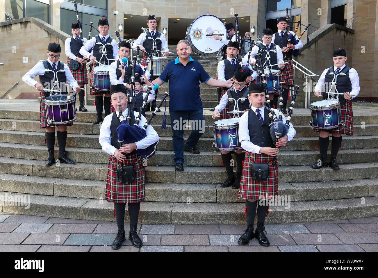 Glasgow, UK. 12th Aug, 2019. Glasgow's international piping festival kicked off today with a special performance by the Scottish Fire and Rescue Novice Juvenile Pipe Band. Now in its 16th year, Piping Live, is the biggest festival of its kind attracting 40,000 music fans, families and fans from around the world to watch more than 5,000 pipers perform at 150 events across the city. Image of RODDY MACLEOD Festival Director, with the band. Credit: Findlay/Alamy Live News Stock Photo