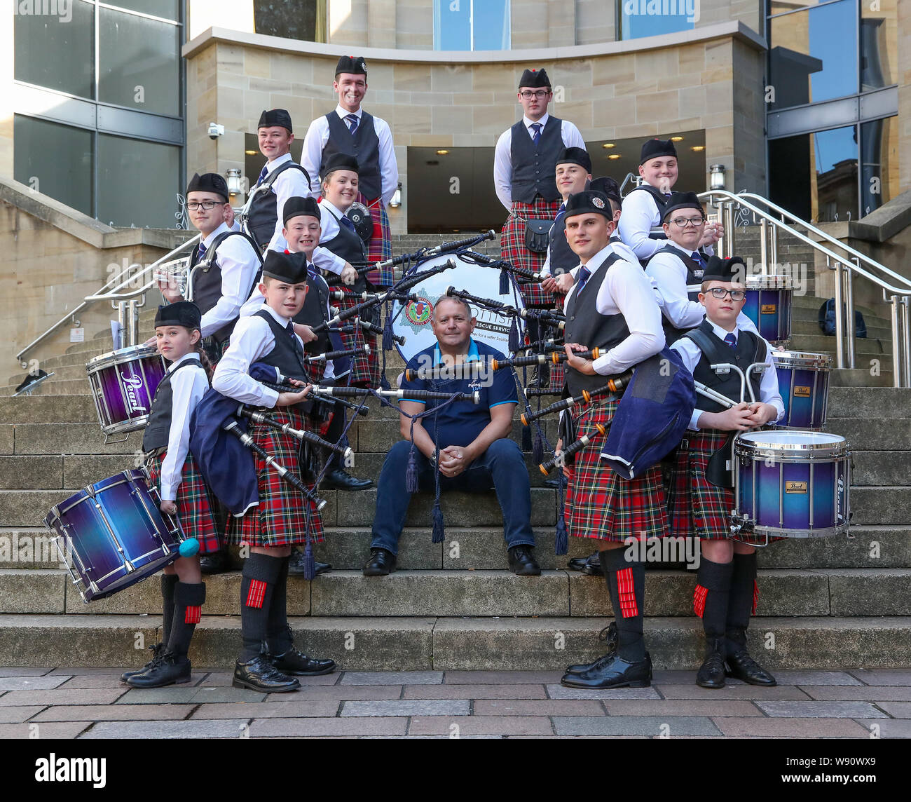 Glasgow, UK. 12th Aug, 2019. Glasgow's international piping festival kicked off today with a special performance by the Scottish Fire and Rescue Novice Juvenile Pipe Band. Now in its 16th year, Piping Live, is the biggest festival of its kind attracting 40,000 music fans, families and fans from around the world to watch more than 5,000 pipers perform at 150 events across the city. Image of RODDY MACLEOD Festival Director, with the band. Credit: Findlay/Alamy Live News Stock Photo