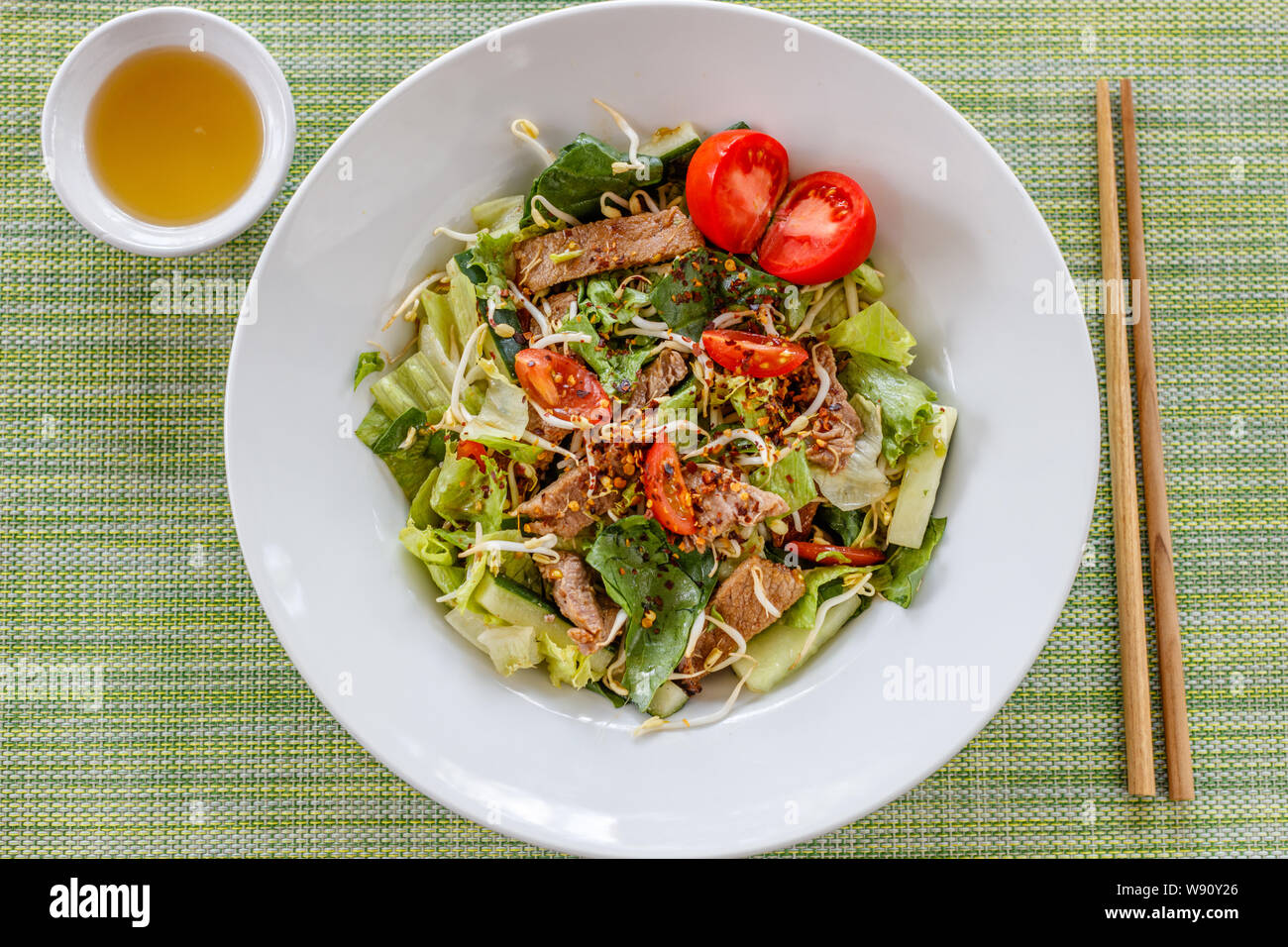 Yam Nuea Yang or Thai beef salad - traditional cuisine of Thailand. Sauce on the side. On green background. Stock Photo