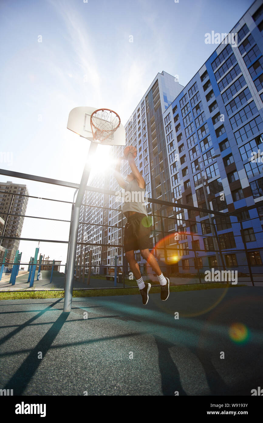 Action shot of African basketball player shooting slam dunk in outdoor court, lens flare Stock Photo