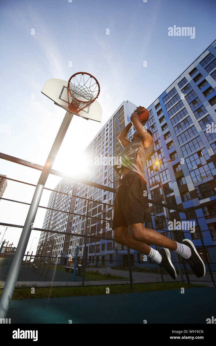 Low angle action shot of African basketball player shooting slam dunk in outdoor court, copy space Stock Photo