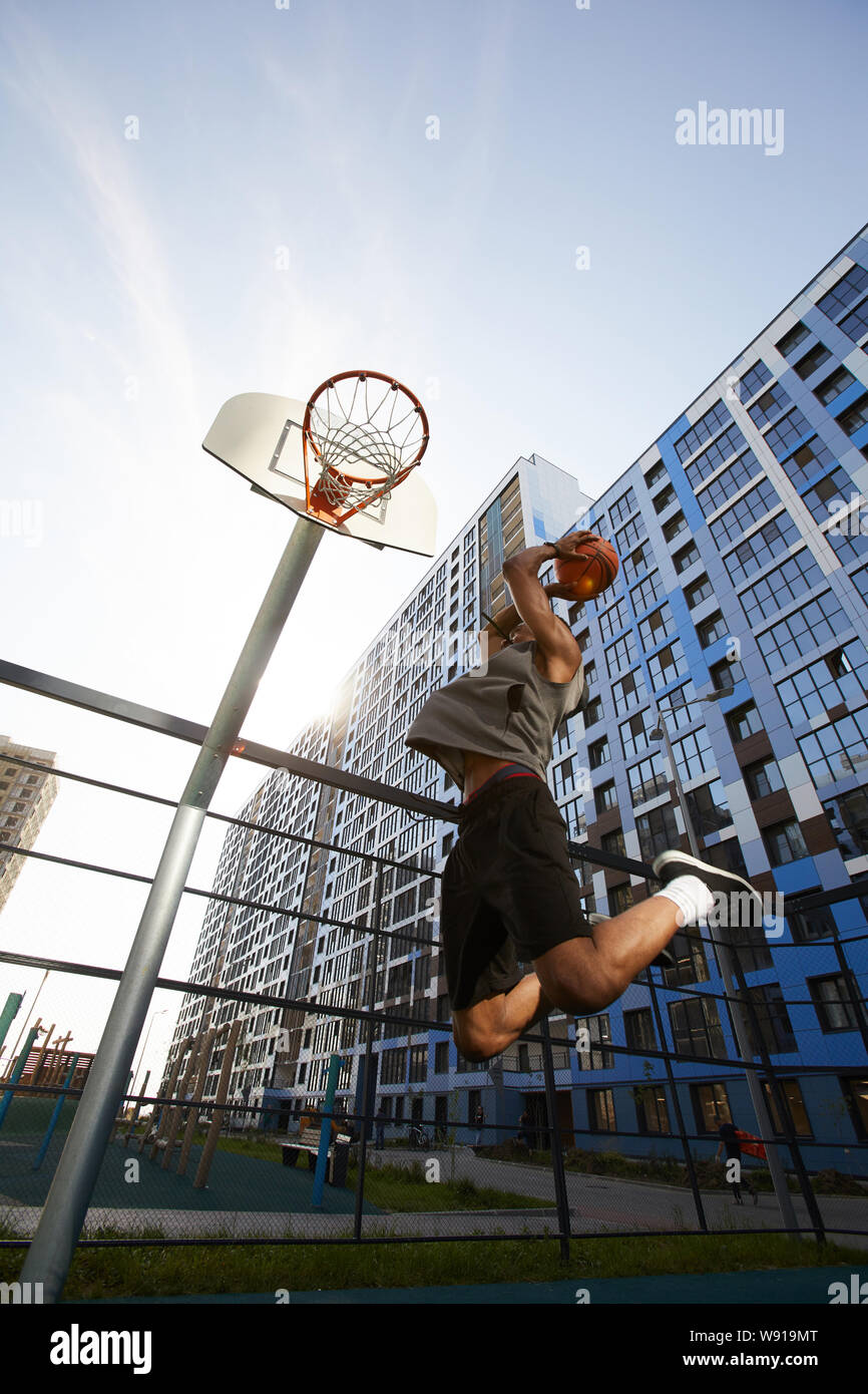 Low angle action shot of African basketball player jumping while shooting slam dunk in outdoor court, copy space Stock Photo