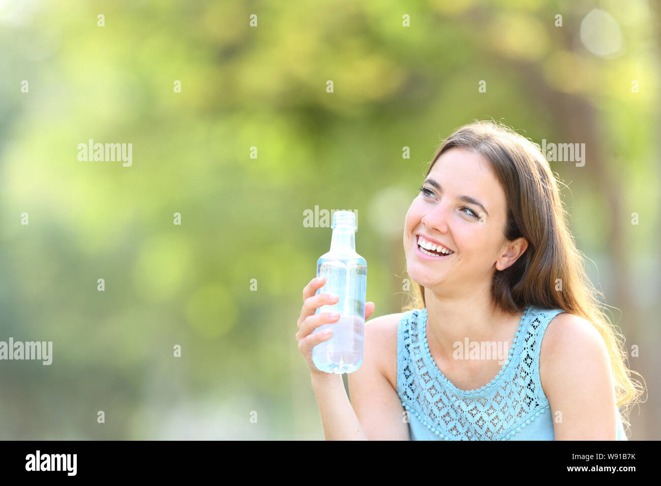 Happy woman holding a water bottle looking at side on green background ...