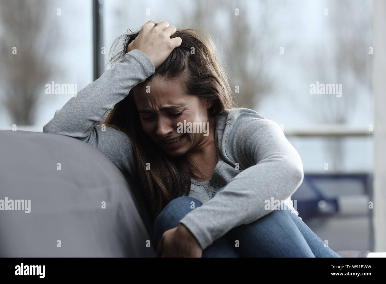 Sad girl complaining and crying alone sitting on a couch in the living room at home Stock Photo