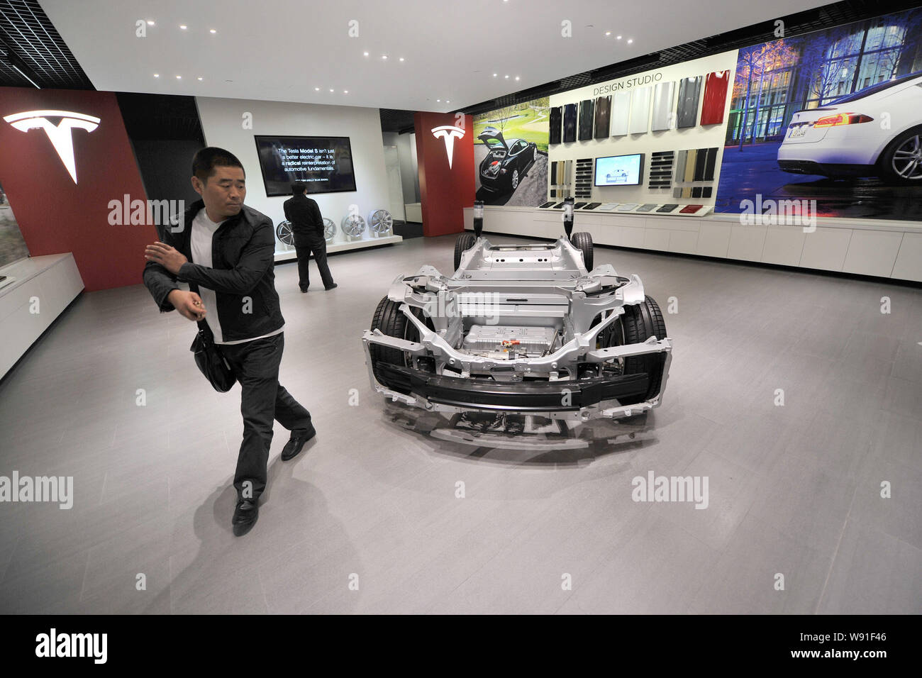 Visitors walk past a chassis of the Model S on dislay at the Tesla store in Beijing, China, 5 November 2013.   US electric carmaker Tesla Motors opene Stock Photo