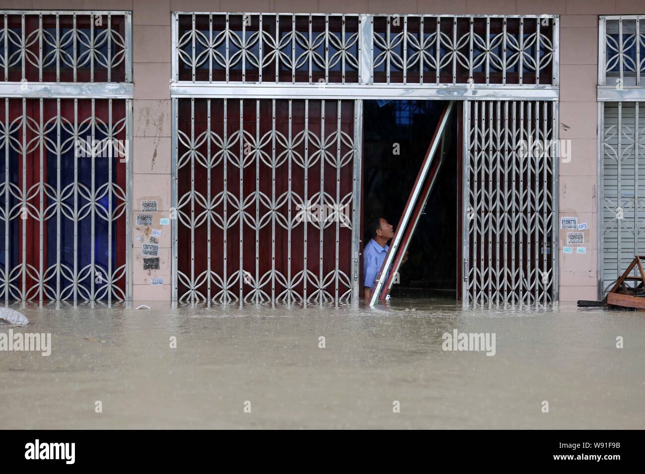 A Chinese man closes the door of his flooded shop after heavy rains caused by Typhoon Fitow in Taoshan town, RuiAn city, east Chinas Zhejiang province Stock Photo