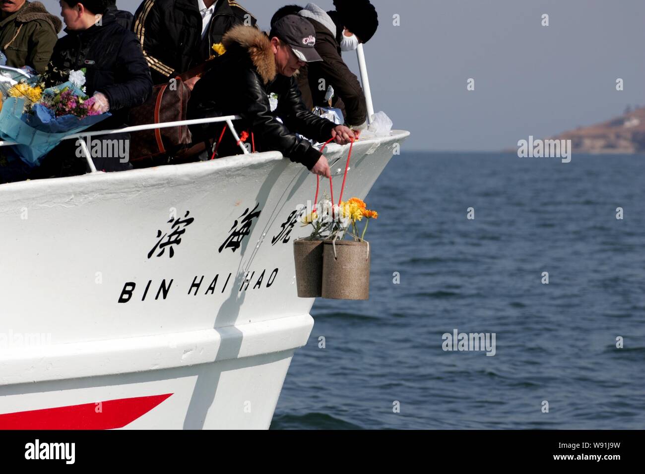 A man lowers the urns with bone ash of a deceased relative before dropping them into the water during a sea burial ceremony on a boat in Dalian city, Stock Photo