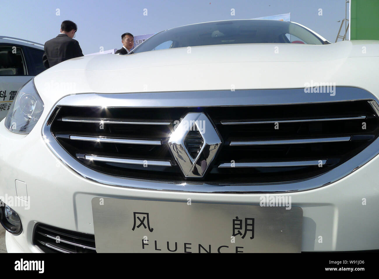 --FILE--Chinese employees stand next to a Renault Fluence during an automobile exhibition in Qingdao, east Chinas Shandong province, 14 April 2013. Stock Photo
