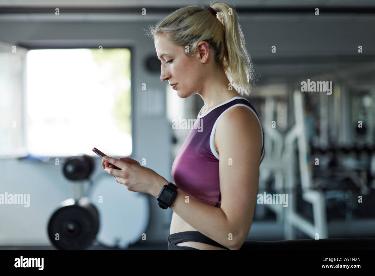 Sporty young woman is looking on her smartphone and reading a text message while training Stock Photo