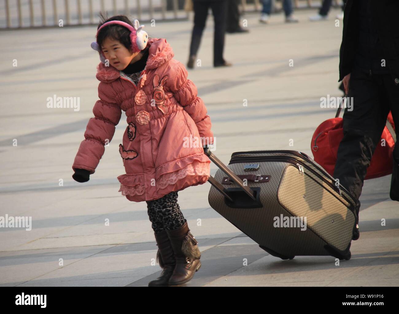 A little girl pulls a big suitcase while walking at Zhengzhou Railway Station as her family prepares to hit the road for home in Zhengzhou, central Ch Stock Photo